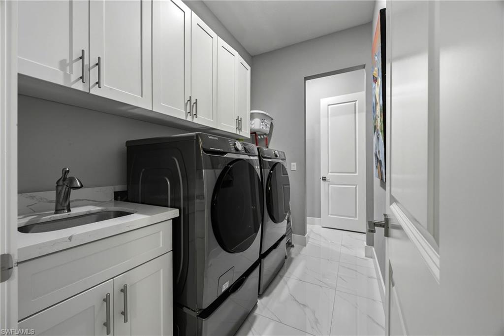 Dedicated laundry space featuring white shaker-style cabinetry, a built-in sink with a countertop, and large format tile flooring