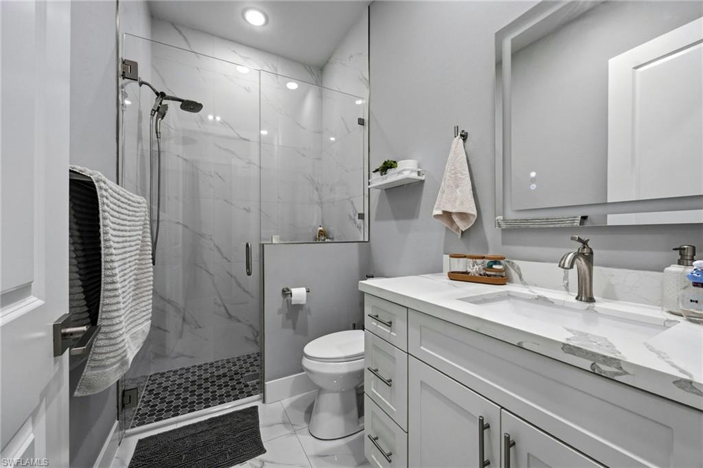 Modern bathroom featuring a glass-enclosed shower with white marble-patterned wall tiling and black mosaic floor tiling