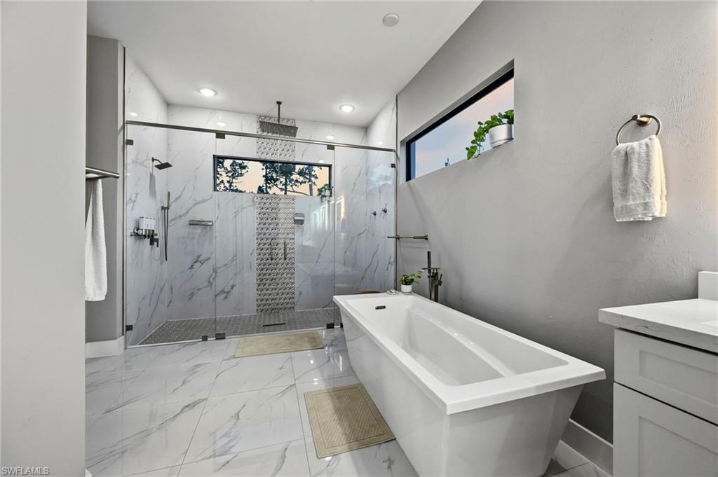 Spacious primary bathroom featuring a frameless glass walk-in shower with dual shower heads, and a freestanding soaking tub