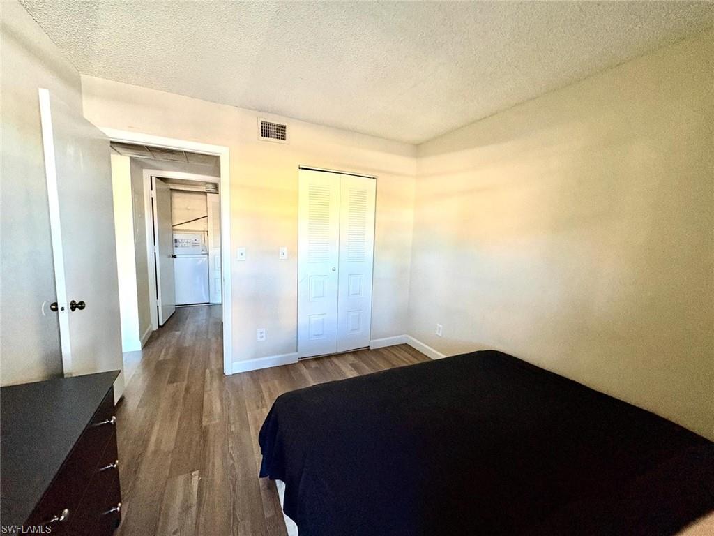 Bedroom with a textured ceiling, dark wood-style floors, a closet, and washer / dryer