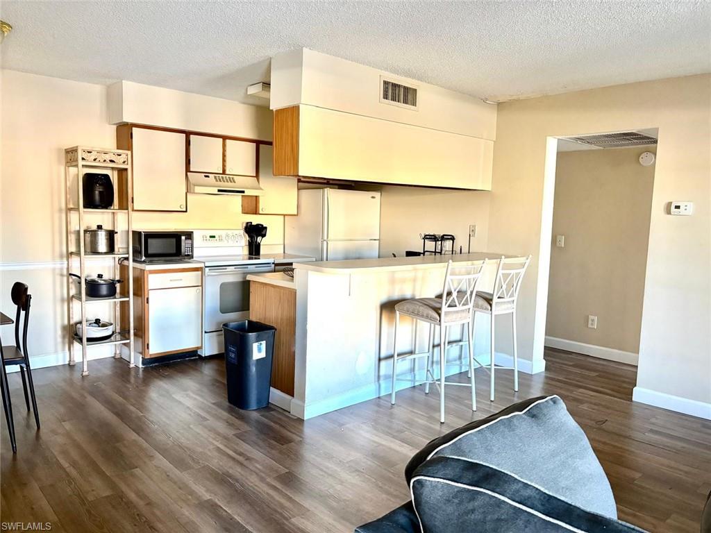 Kitchen with light countertops, white appliances, a textured ceiling, a breakfast bar, and brown cabinets