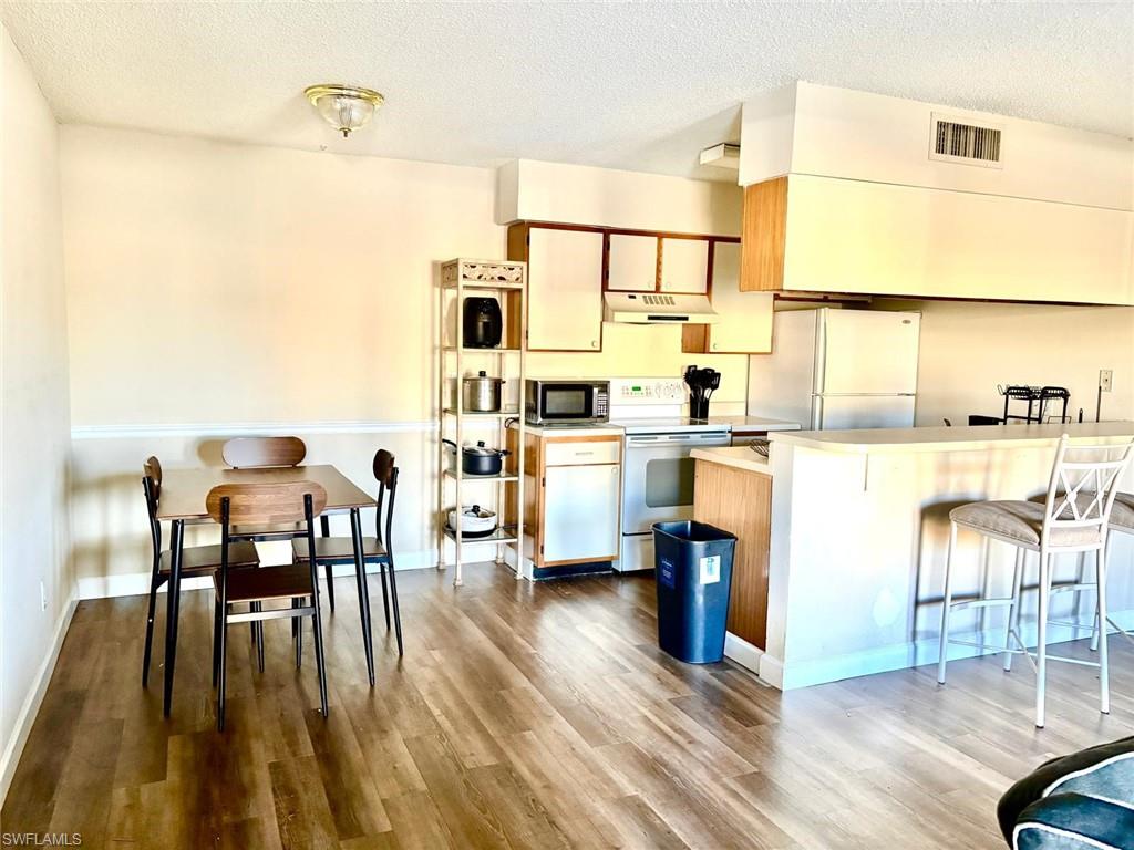Kitchen featuring light countertops, a textured ceiling, white appliances, a kitchen bar, and under cabinet range hood