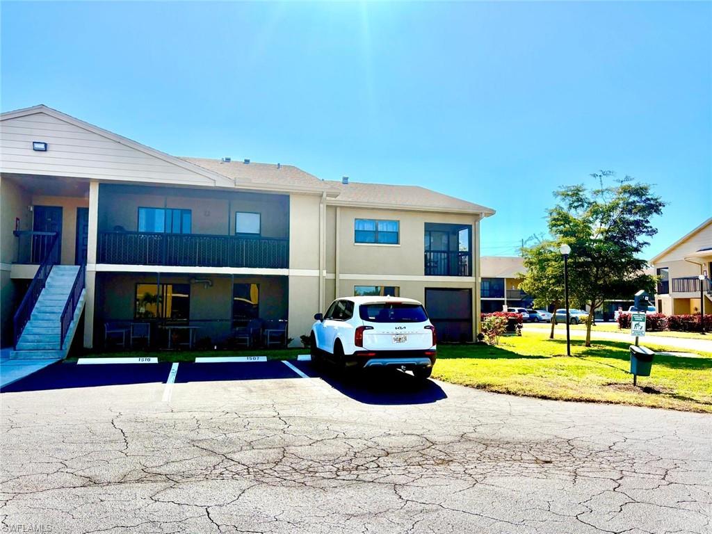 View of front of house with uncovered parking, stairs, a front lawn, and stucco siding