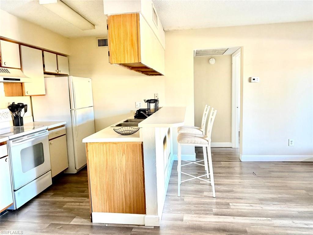 Kitchen with white appliances, a kitchen breakfast bar, light countertops, light wood-style floors, and a textured ceiling