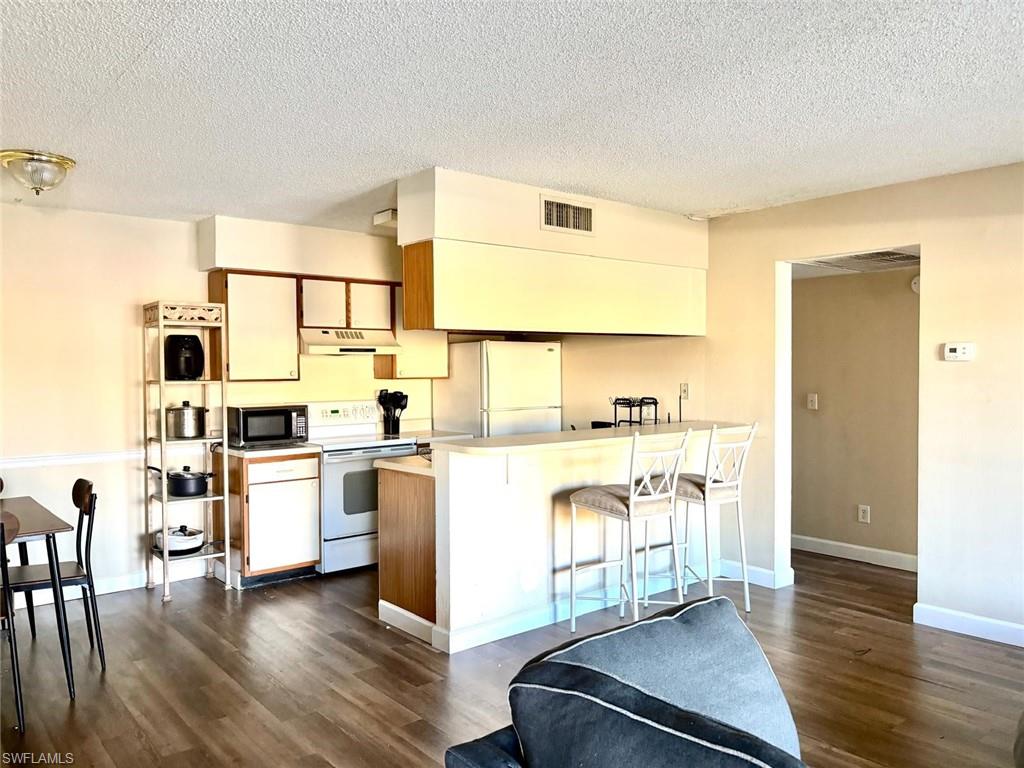Kitchen with light countertops, brown cabinets, white appliances, a breakfast bar, and a textured ceiling