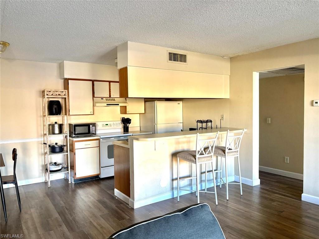 Kitchen featuring white electric range, freestanding refrigerator, a breakfast bar area, light countertops, and a textured ceiling