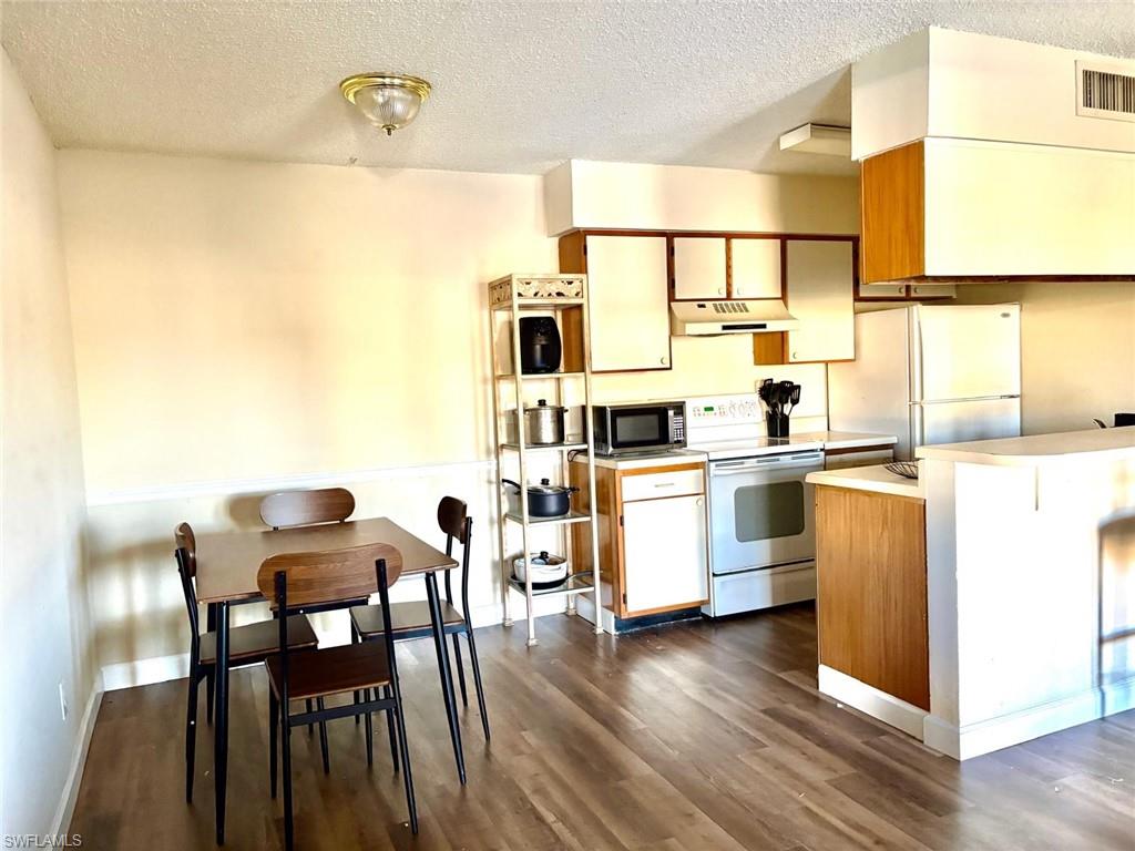 Kitchen with brown cabinetry, light countertops, electric stove, freestanding refrigerator, and a textured ceiling
