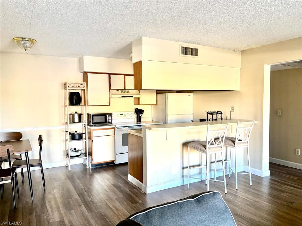 Kitchen with a breakfast bar area, white appliances, light countertops, a textured ceiling, and dark wood-style floors