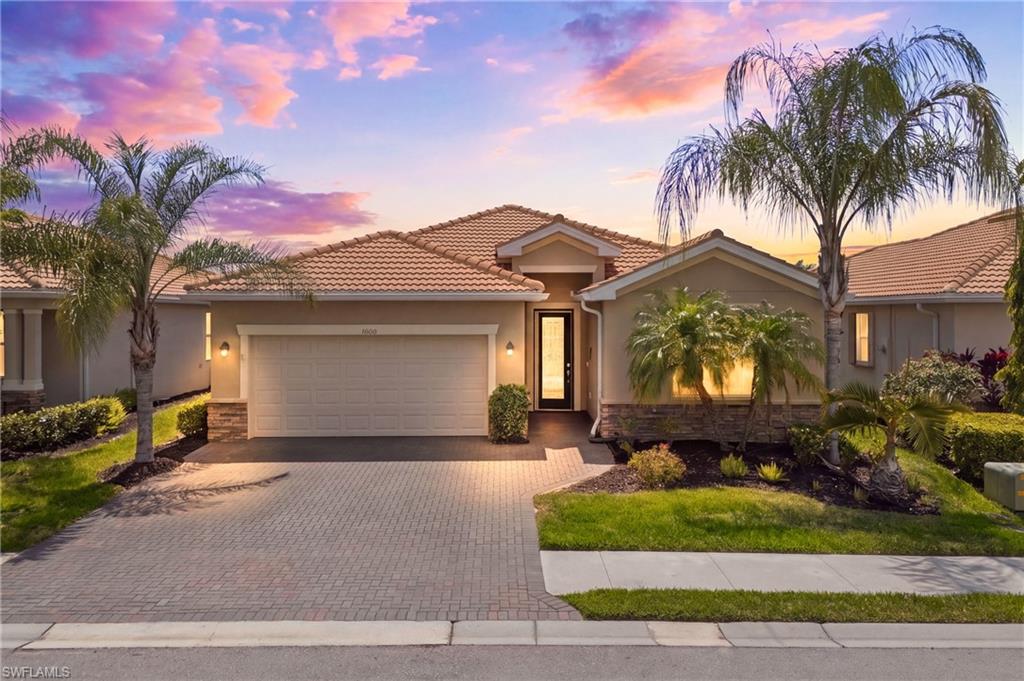 Stunning front elevation framed by a glowing sunset sky, showcasing beautiful landscaping and inviting curb appeal in Pelican Preserve.