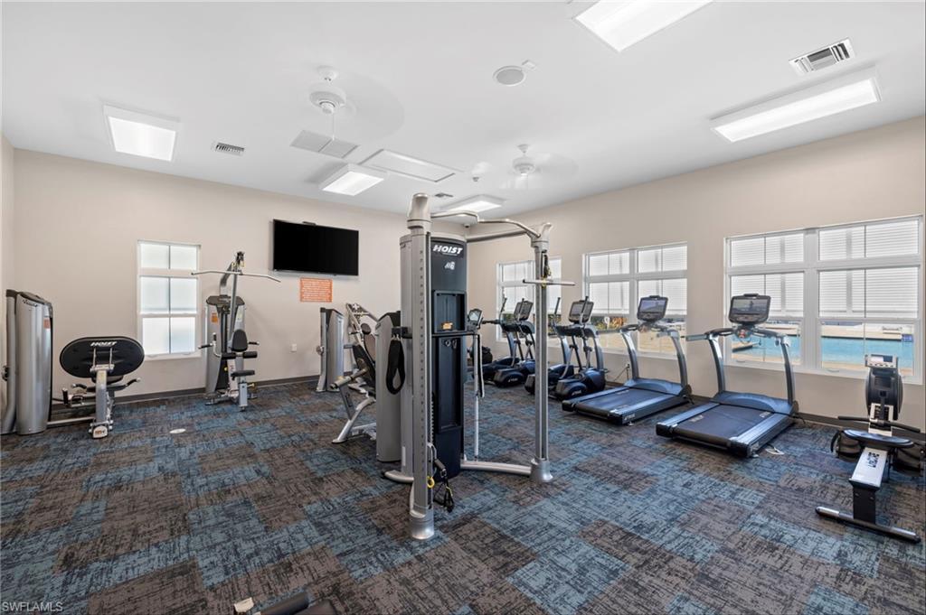 Fitness center featuring patterned carpet flooring, multiple windows with blinds, recessed lighting, and ceiling fans