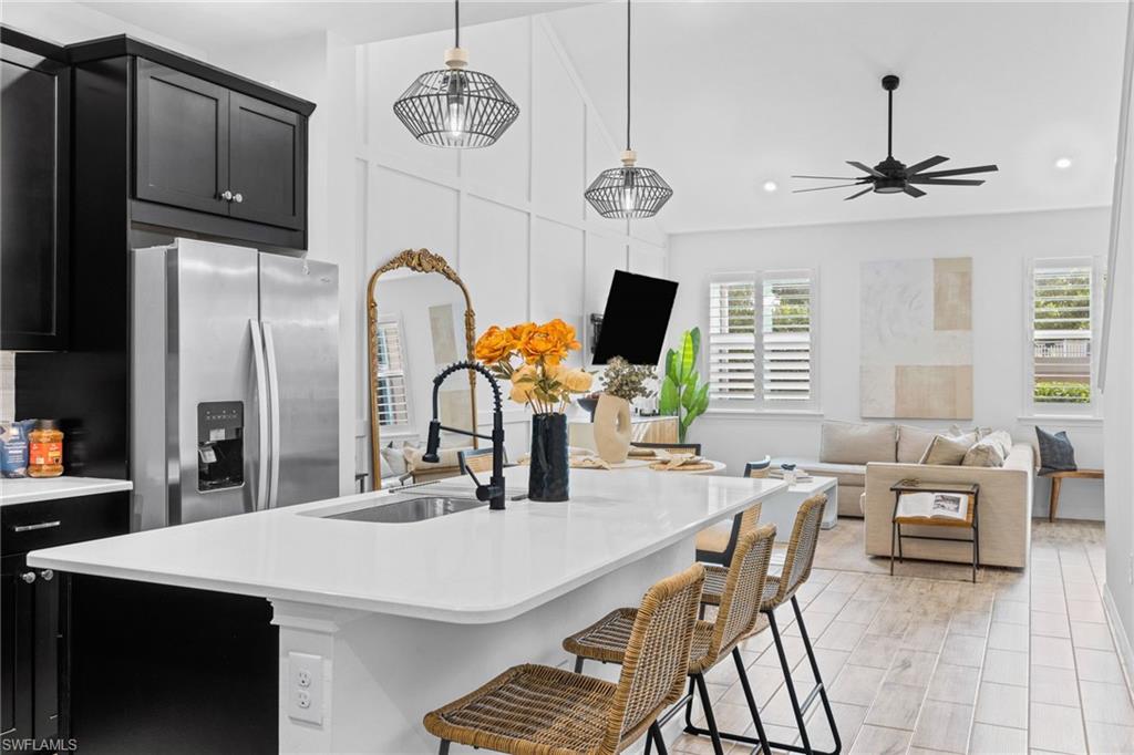Open-concept living space featuring a kitchen island with a built-in sink, white countertops, black cabinetry, and a full-size stainless steel refrigerator