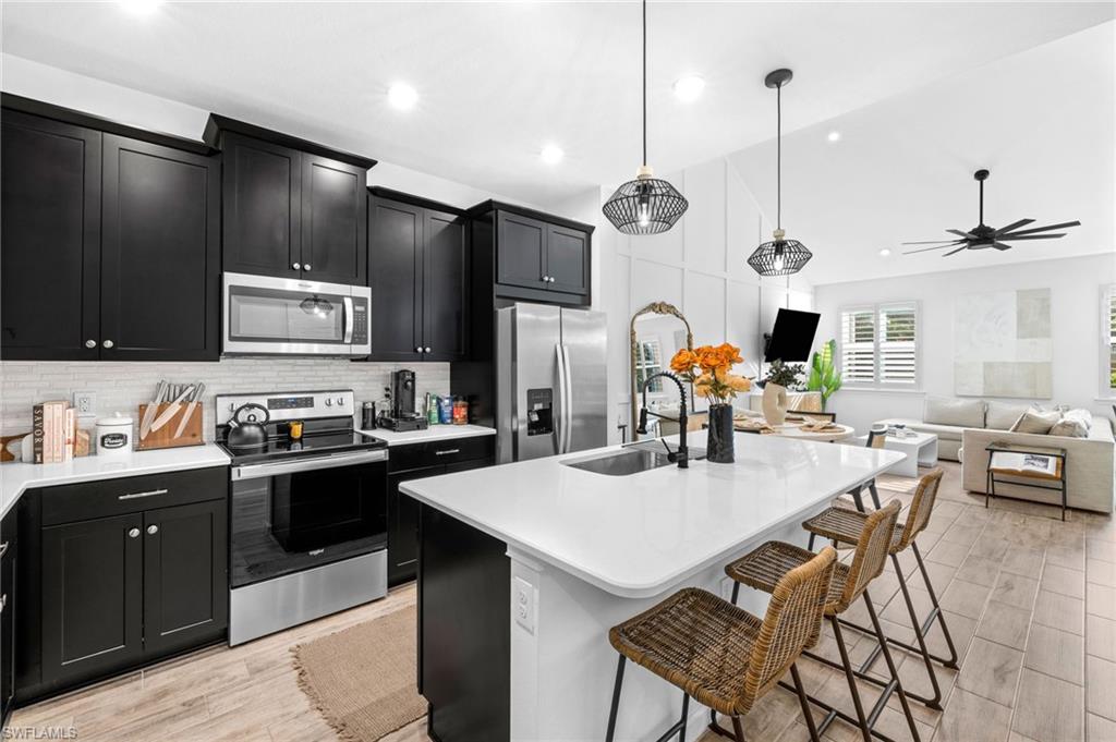 Open-concept kitchen featuring black cabinetry, stainless steel appliances, a white subway tile backsplash, and a large central island with a sink and seating