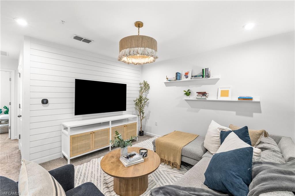 Living space with shiplap accent wall, recessed lighting, and a gold-finish drum chandelier