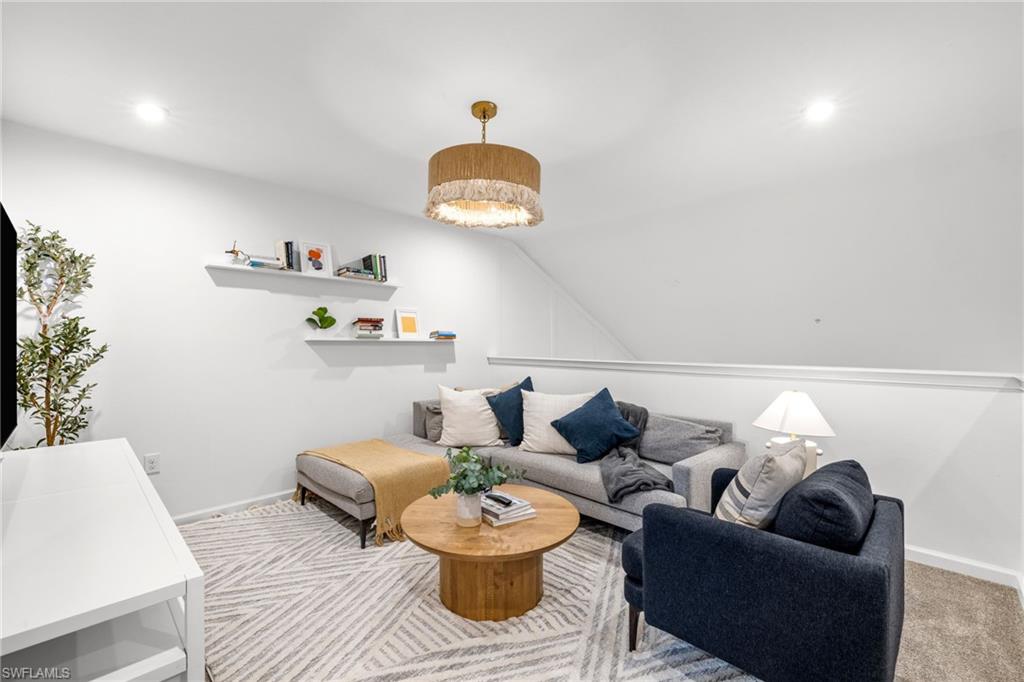 Carpeted living area featuring a decorative ceiling light fixture, recessed lighting, and a partial wall with a cap rail