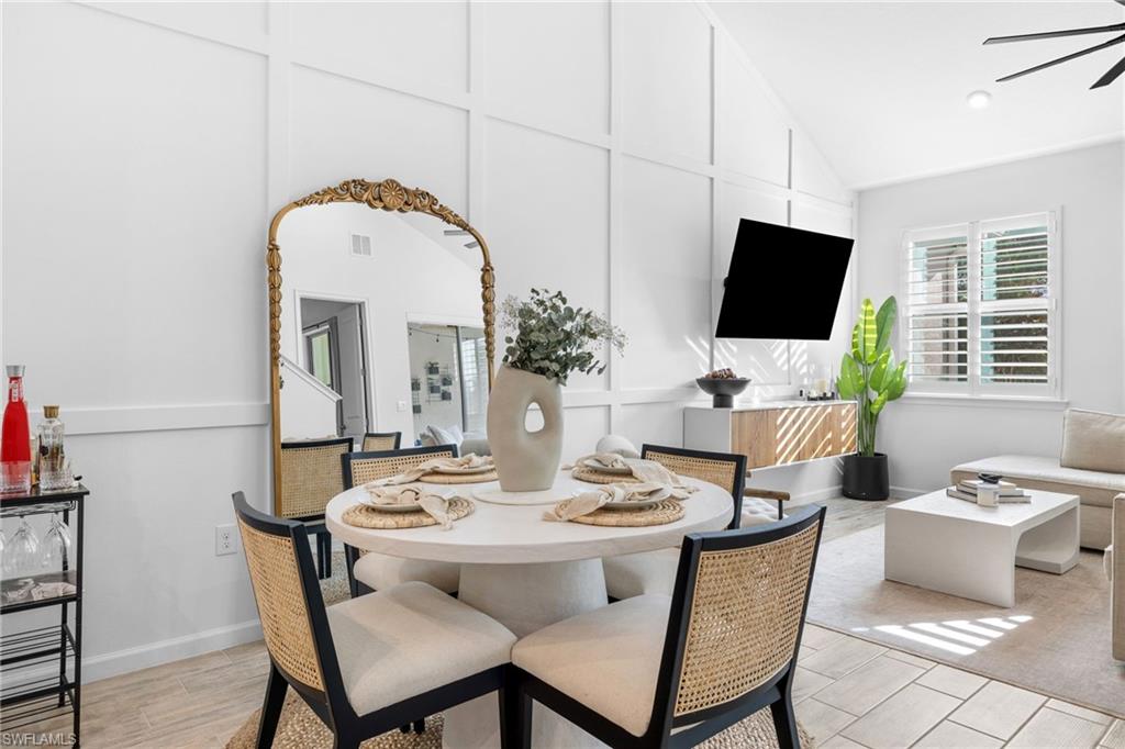 Open-concept dining and living area featuring vaulted ceilings, board and batten accent wall, wood-finish flooring, and plantation shutters