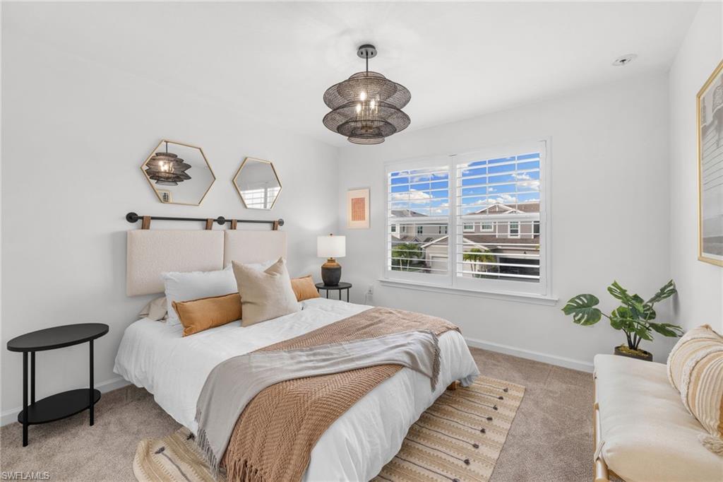 Bedroom featuring a window with white louvered shutters, carpet flooring, a multi-tiered circular ceiling light fixture, and light-colored walls
