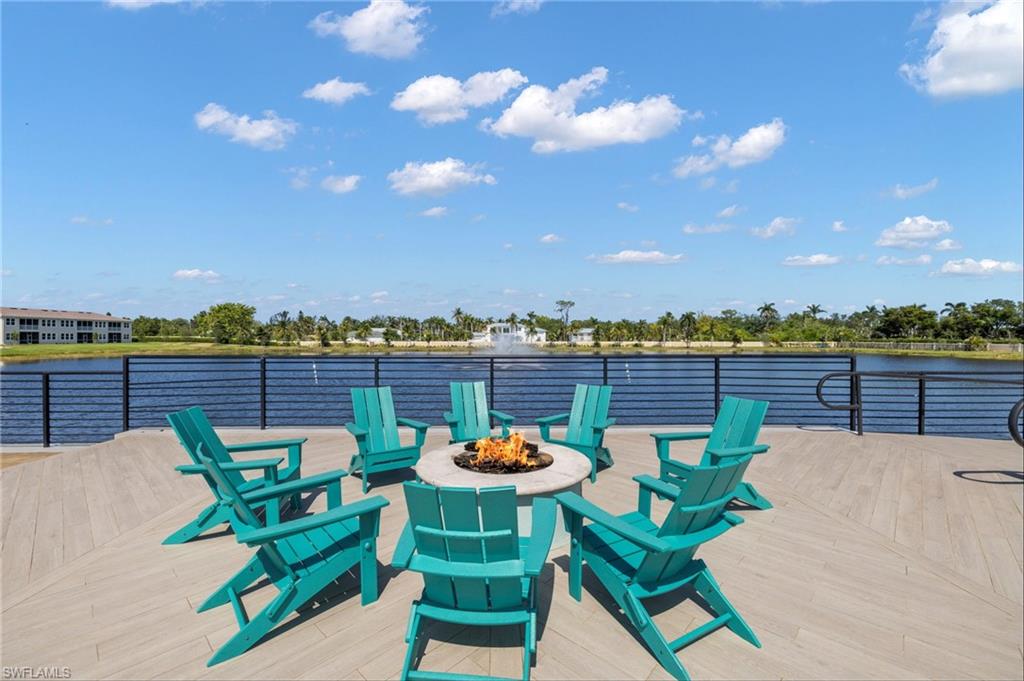 Expansive waterfront patio featuring wood-finish decking, a built-in circular fire pit, and a black horizontal bar railing
