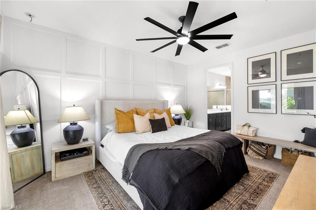 Bedroom featuring a contemporary black ceiling fan, white paneled accent wall, neutral carpeting, and an ensuite bathroom entrance with a double vanity