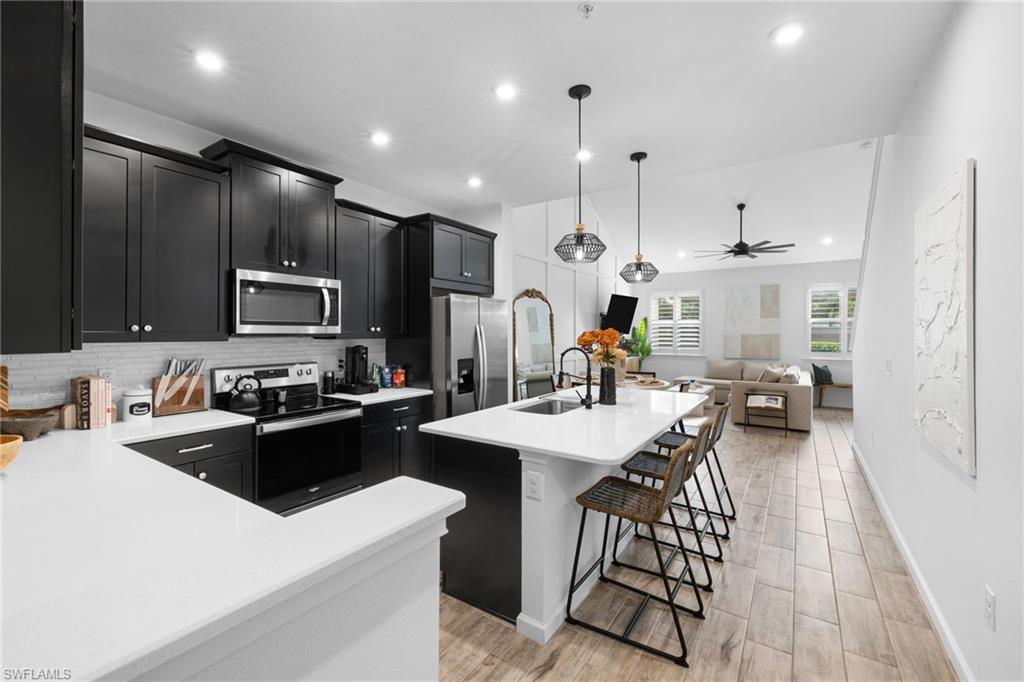 Modern kitchen featuring dark cabinetry, white countertops, stainless steel appliances, and a tile backsplash