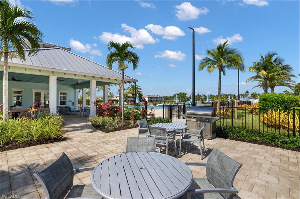 Spacious paver patio area featuring a built-in grill station and multiple seating arrangements, surrounded by lush landscaping and palm trees