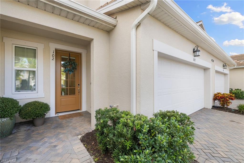 Stucco exterior featuring a transom window above the wood-finish front door, complemented by a paver walkway and multiple garage doors