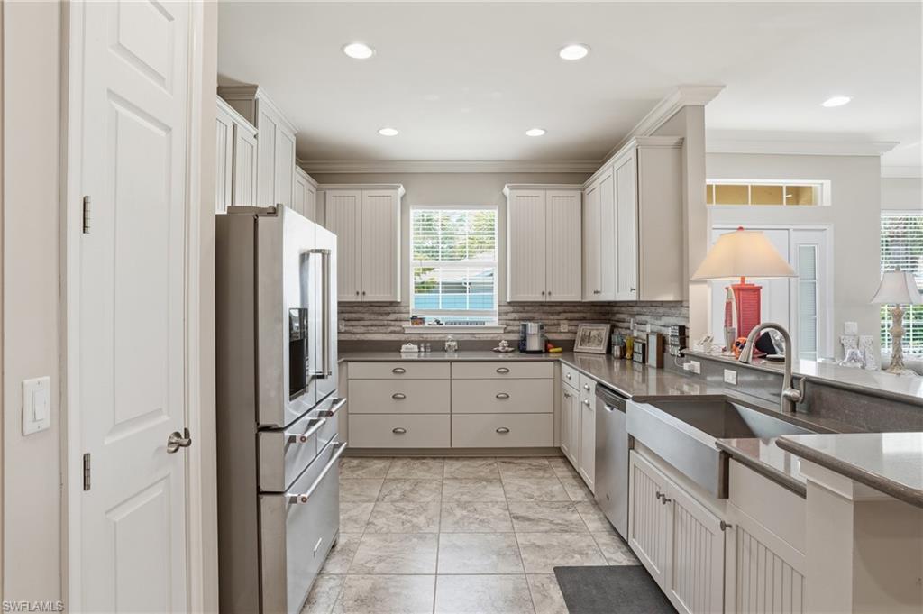Spacious kitchen featuring white cabinetry, stainless steel appliances, a farmhouse sink, stone countertops, and a tile backsplash
