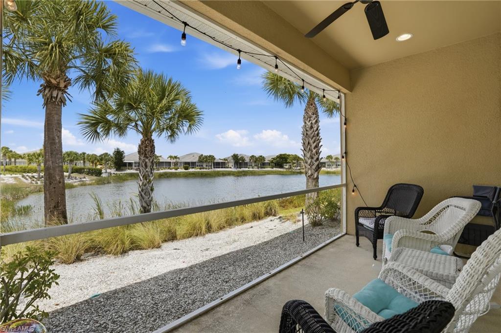 Screened porch with concrete flooring and a ceiling fan, overlooking a body of water with established palm trees and natural landscaping