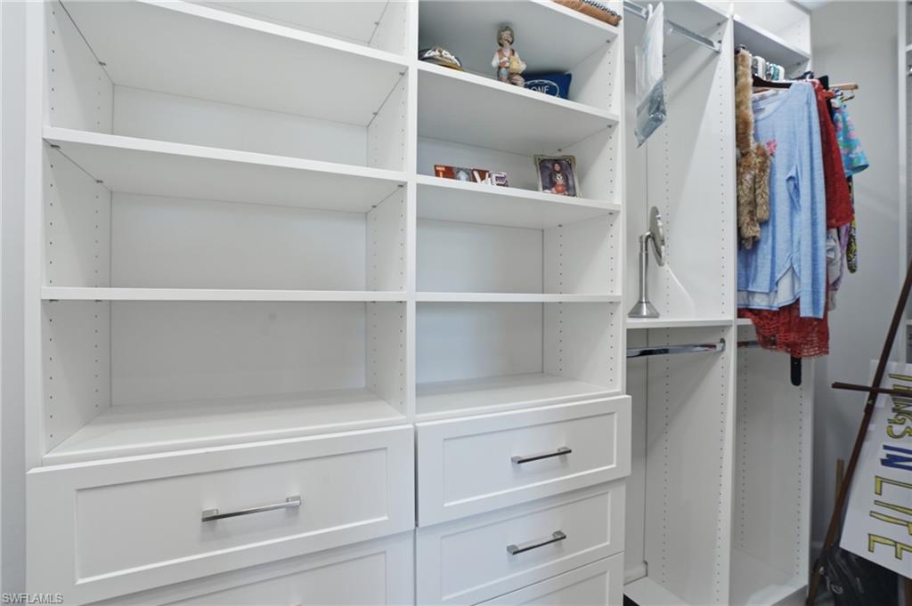 Custom closet system featuring white built-in shelving, multiple hanging rods, and pull-out drawers with chrome hardware