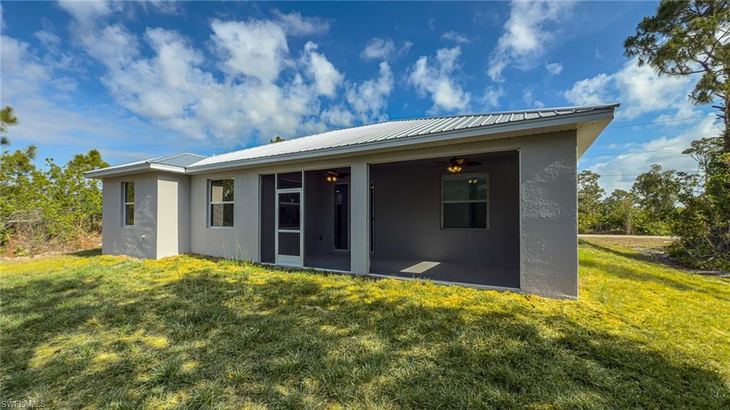 Back of house with a yard, a sunroom, metal roof, and stucco siding