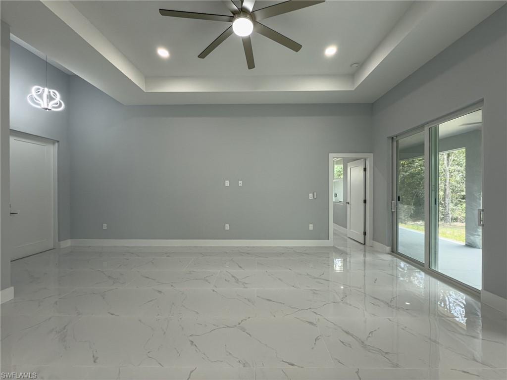 Spare room featuring ceiling fan, a tray ceiling, marble finish floor, and baseboards