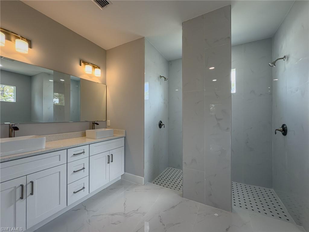 Bathroom with visible vents, a walk in shower, double vanity, and a sink