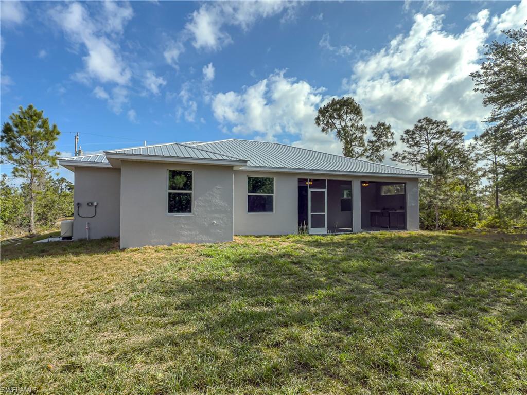 Rear view of property with a sunroom, stucco siding, metal roof, and a yard