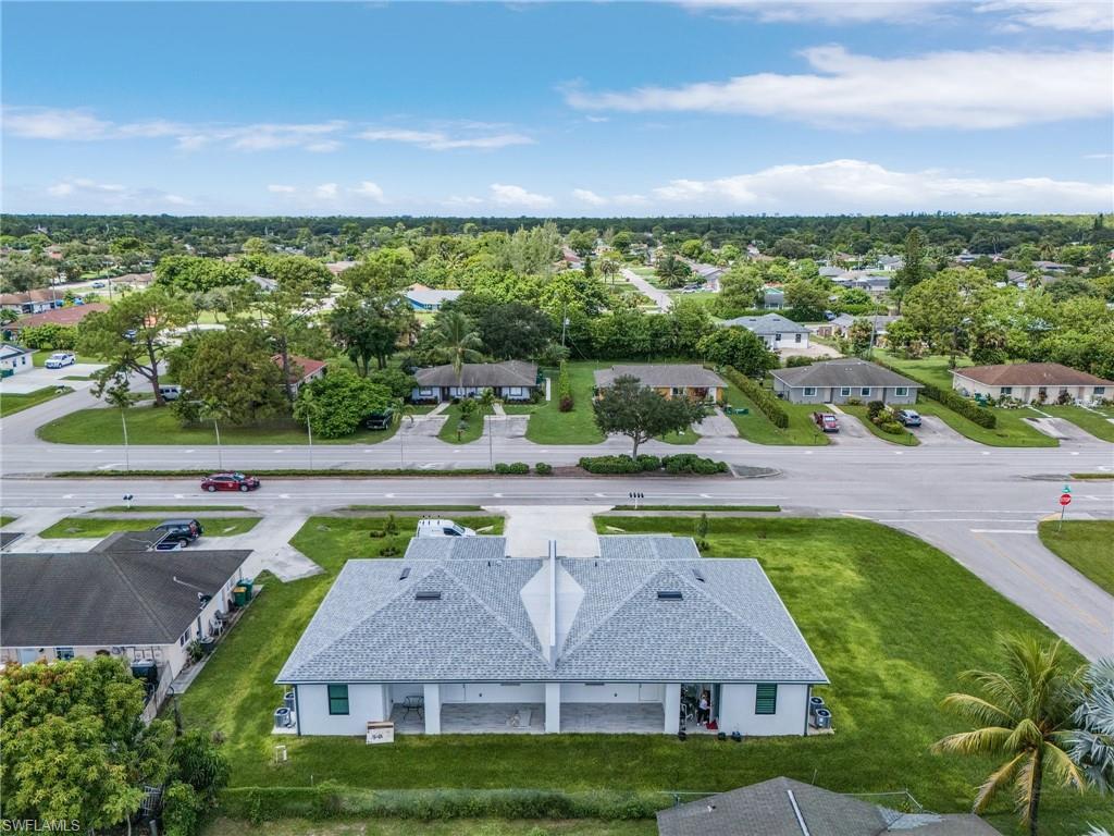 Duplex property featuring a light gray shingle roof, white exterior siding, covered parking, and an expansive green lawn