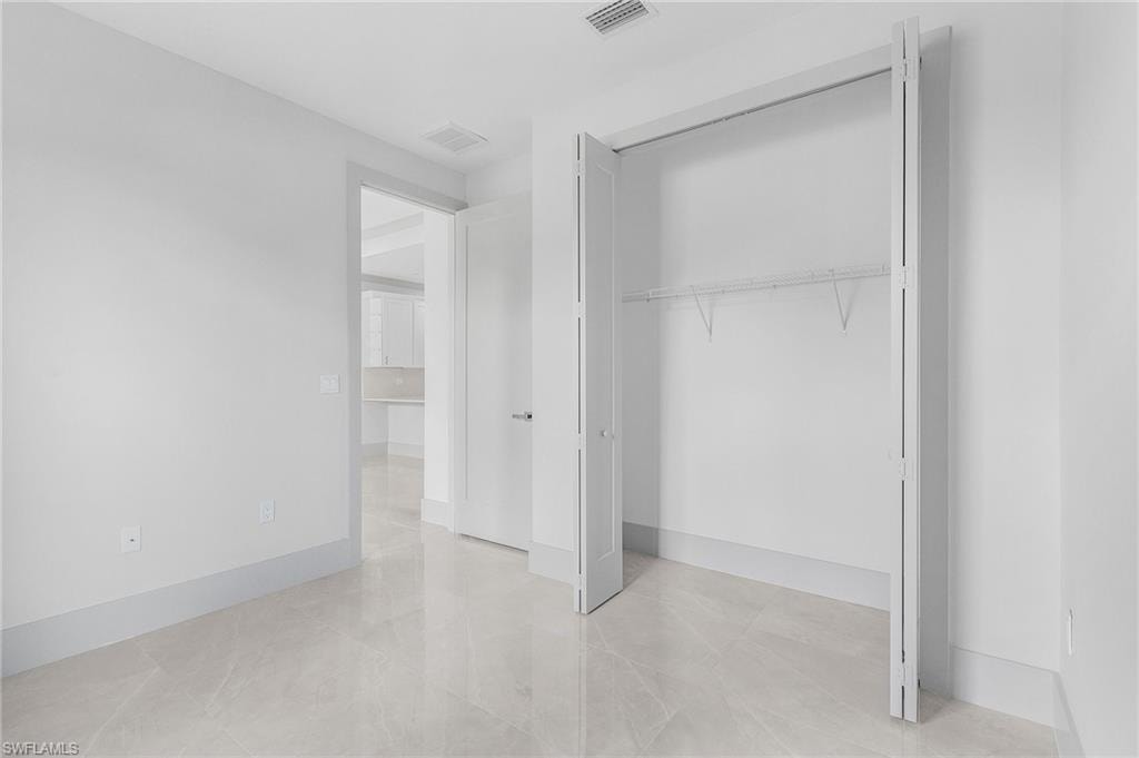 Room featuring light-toned large format tile flooring, white painted walls, and a bi-fold closet with shelving