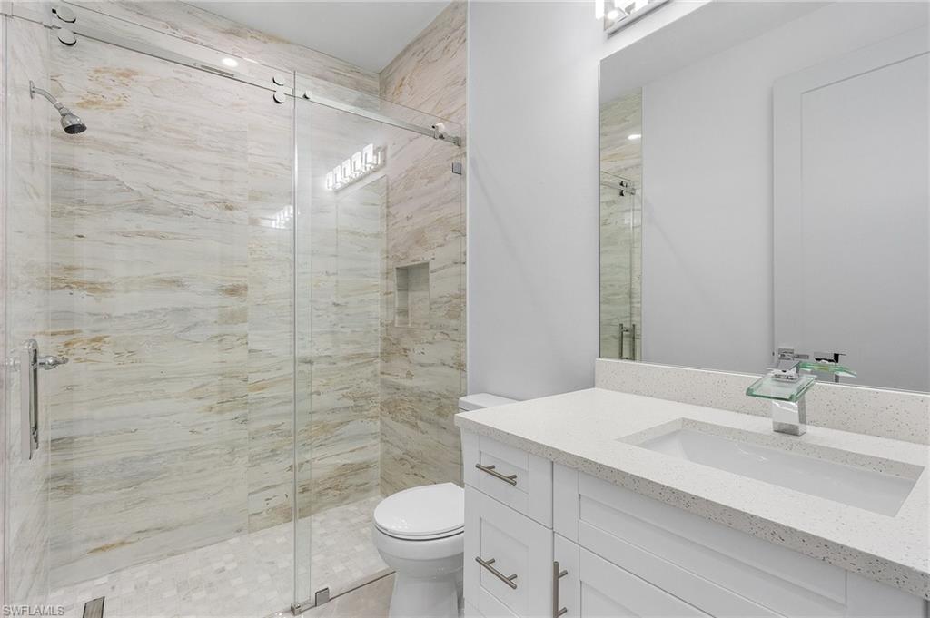 Contemporary bathroom featuring a frameless glass shower enclosure with a rain showerhead, a built-in shower niche, and large format natural stone-look wall tiles