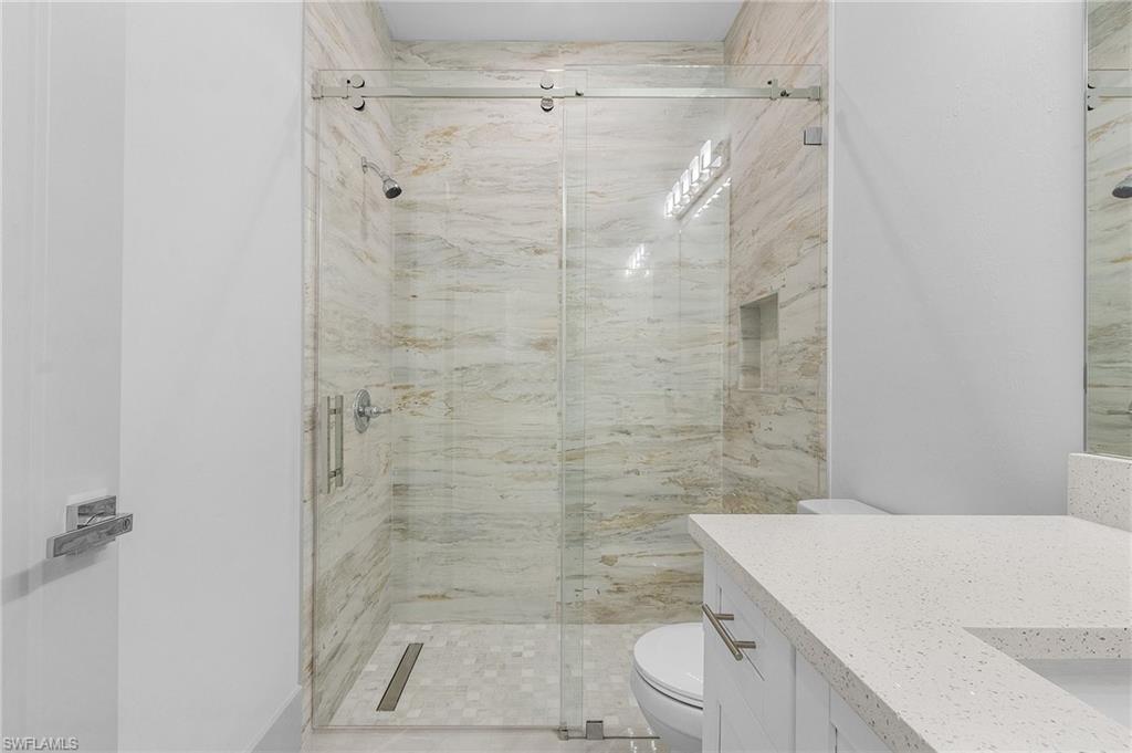 Walk-in shower featuring a frameless glass enclosure, natural stone-finish wall tile, hexagonal floor tile, and a built-in shower niche