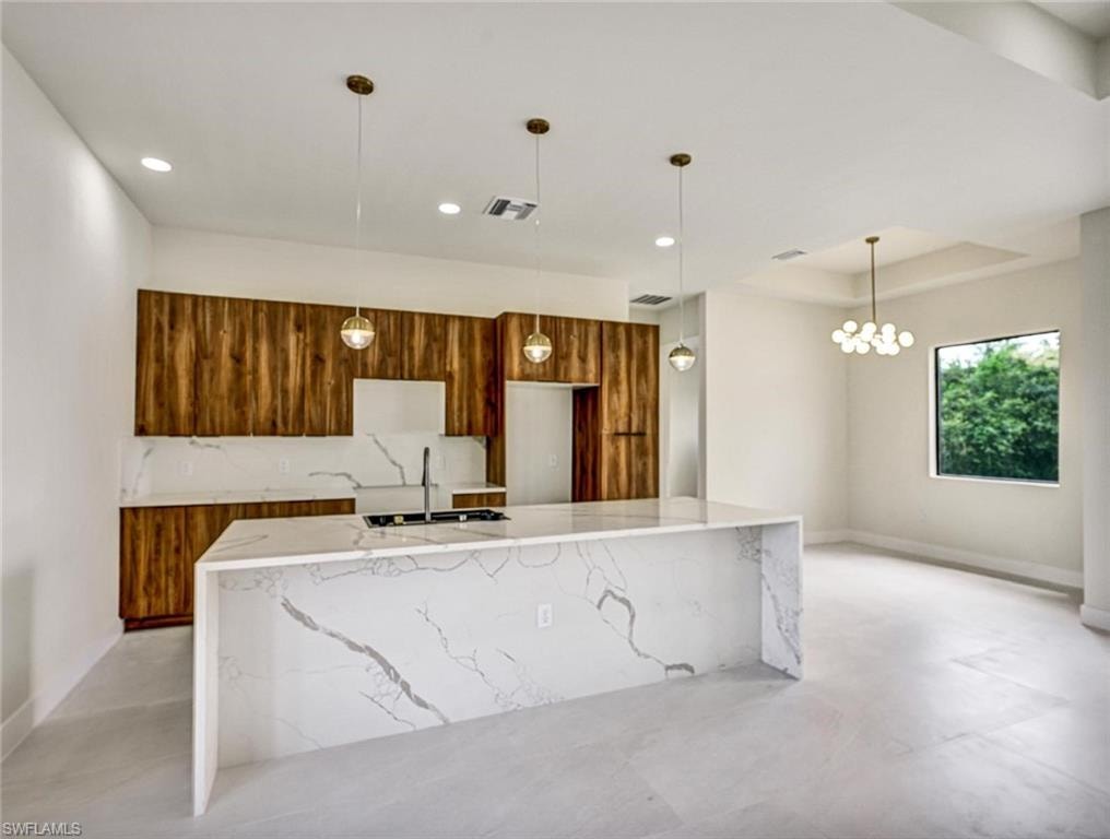 Kitchen featuring a waterfall-edge island with integrated sink, wood-finish cabinetry, patterned backsplash, and recessed and pendant lighting