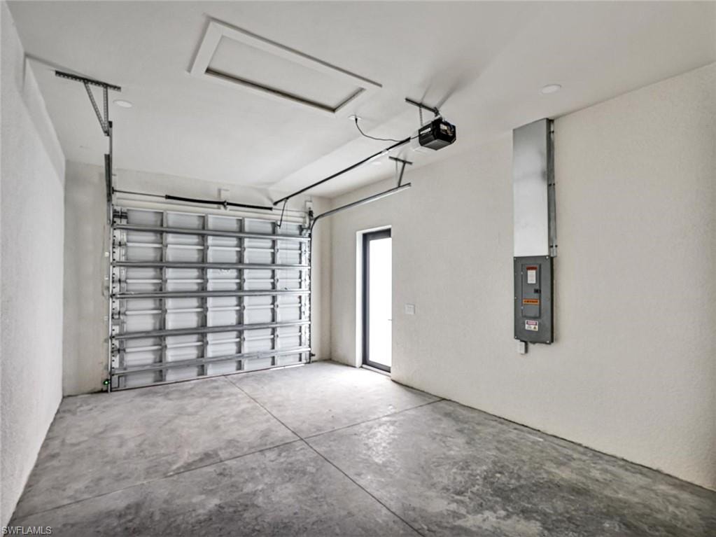 Spacious garage featuring a concrete floor, a roll-up garage door, a side entry door, and an overhead lighting fixture