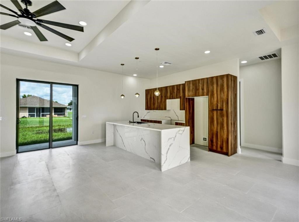 Open-concept living space with large sliding glass doors, a kitchen island featuring a waterfall edge, wood-finish cabinetry, and recessed lighting