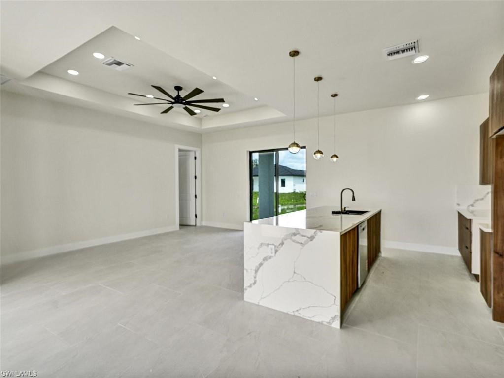 Open-concept area featuring a waterfall kitchen island with integrated sink, wood-finish cabinetry, and pendant lighting