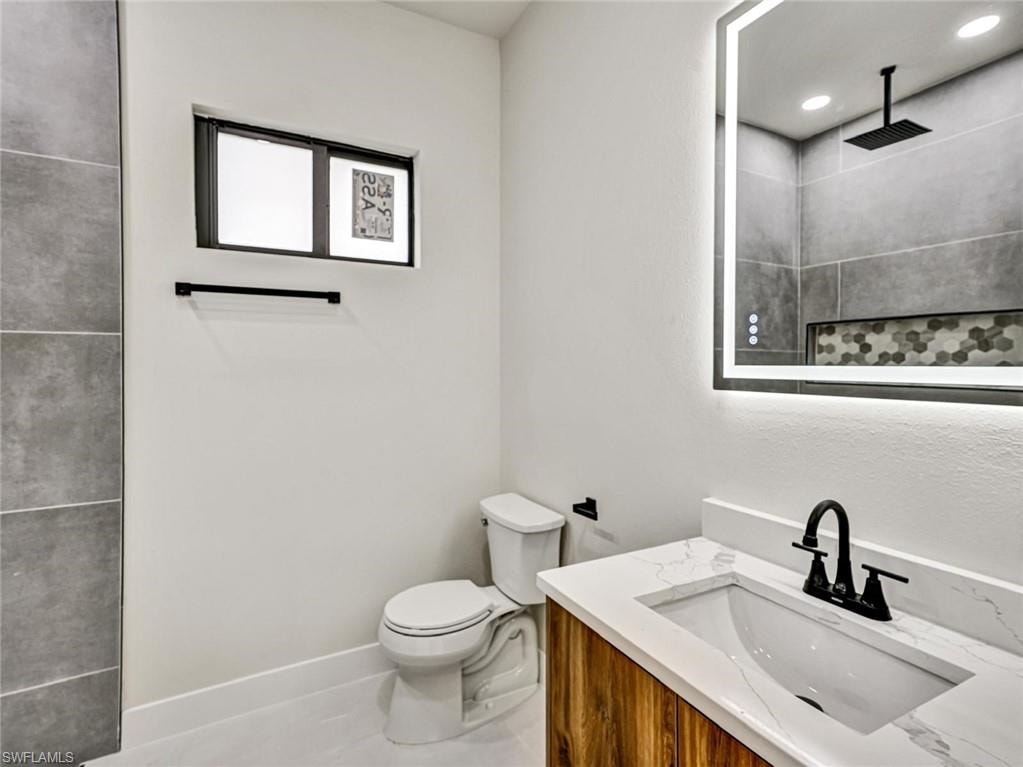 Modern bathroom featuring a wood-finish vanity with a white countertop and integrated sink, a backlit mirror, and a shower with grey large-format tile and a hexagon mosaic accent
