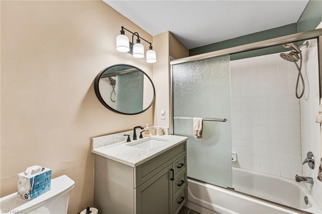 The second full bathroom features a shower and tub combination enclosed in elegant rain glass, complemented by a single granite-topped vanity that adds a refined touch of sophistication.