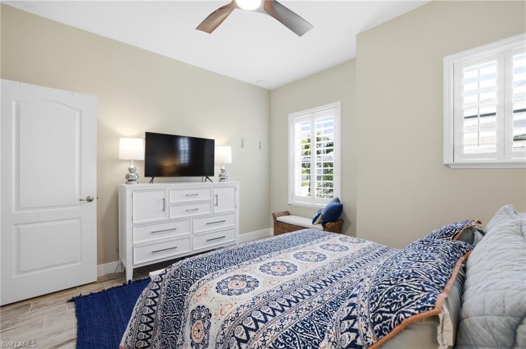 Bedroom featuring wood-finish flooring, two large windows with white plantation shutters, a ceiling fan, and light-toned wall paint