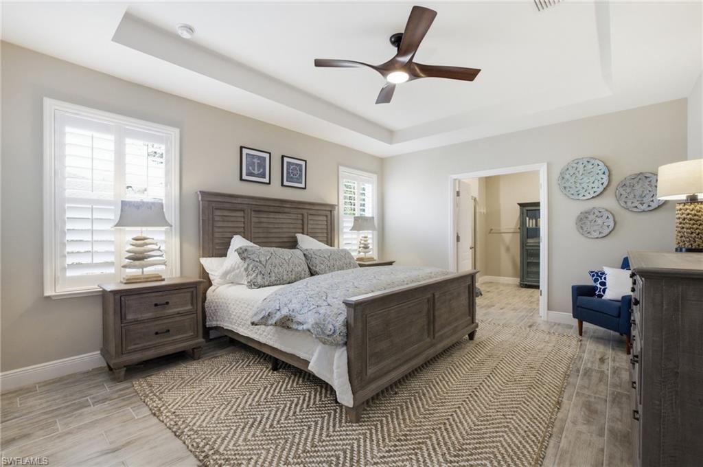 Spacious room featuring a tray ceiling with a modern ceiling fan, plantation shutters, and wood-finish tile flooring