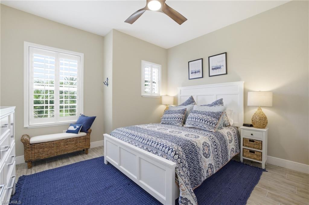 Bedroom featuring wood-finish flooring, a white paneled bed frame, and a ceiling fan with wood-tone blades
