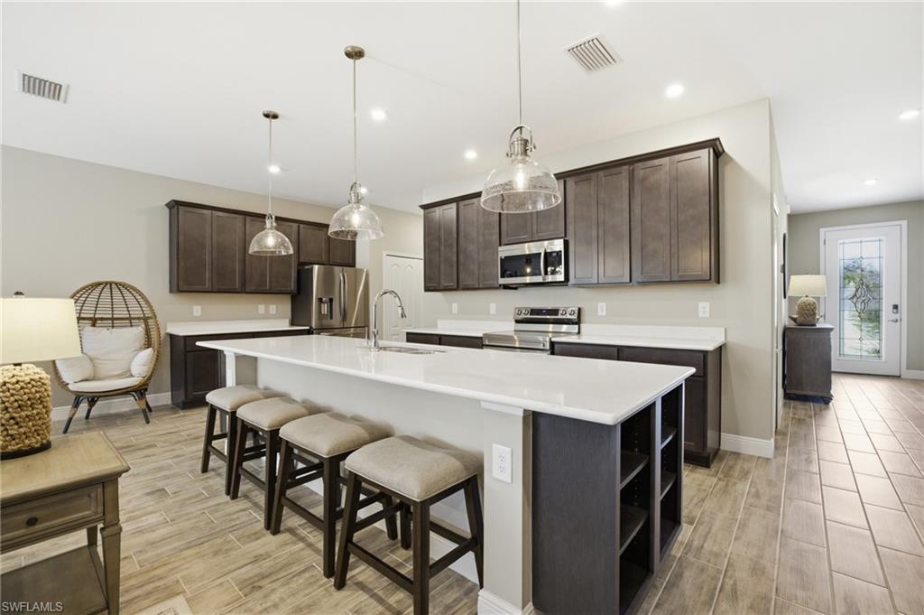 Kitchen featuring a large central island with seating, dark wood cabinetry, stainless steel appliances, and white countertops