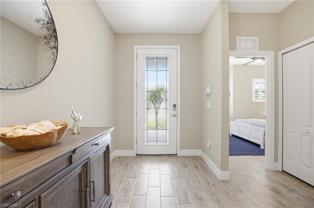 Inviting entryway featuring wood-finish tile flooring, a white paneled door with decorative glass inserts, and a built-in storage cabinet with dark hardware