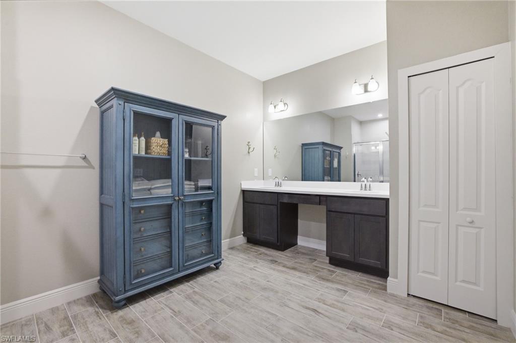 Spacious bathroom featuring wood-finish tile flooring, a dual vanity with white countertops, and a large wall mirror