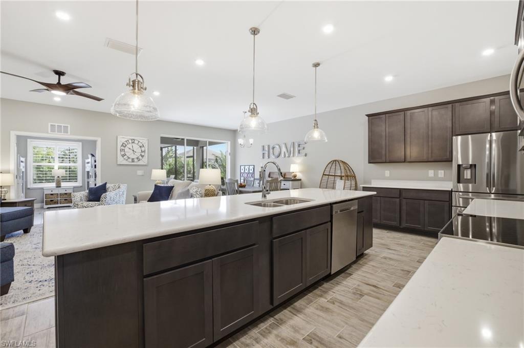 Open-concept kitchen featuring an oversized island with double sink, stainless steel appliances, dark wood cabinetry, white countertops, and wood-finish flooring