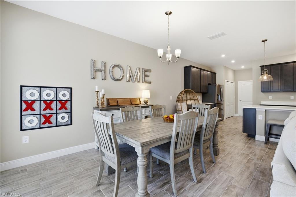 Open-concept living space featuring wood-finish tile flooring throughout, a dining area with a chandelier, and a kitchen with dark cabinetry and light countertops